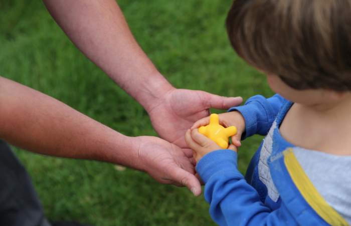 a kid taking a yellow toy from an adults hands