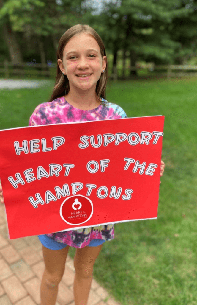 A woman holding the board help support heart of the hamptons